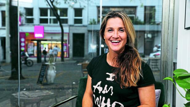 Eine lächelnde Frau sitzt in einem Café mit Blick auf die Straße.