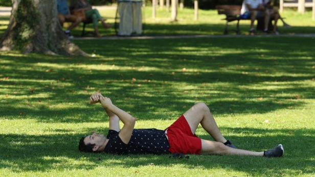 Ein Mann liegt entspannt im Gras eines Parks.