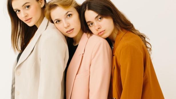 Stilvolle junge Frauen in pastellfarbenen Outfits stehen zusammen, Modekonzept.