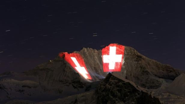 Die Schweizer Flagge wird nachts auf einen Berg projiziert.
