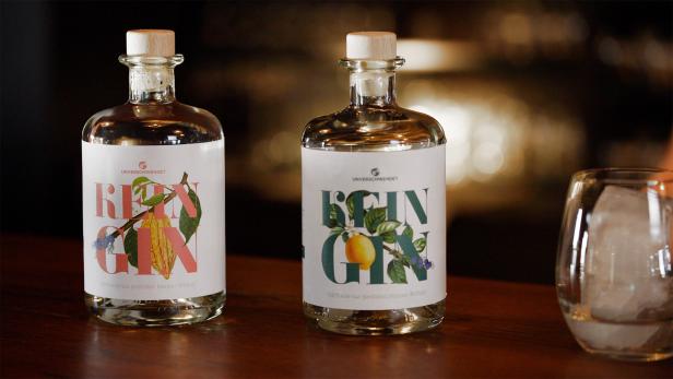 Zwei Flaschen „Unverschwendet Rein Gin“ und ein Glas mit Eiswürfeln auf einem Tisch.