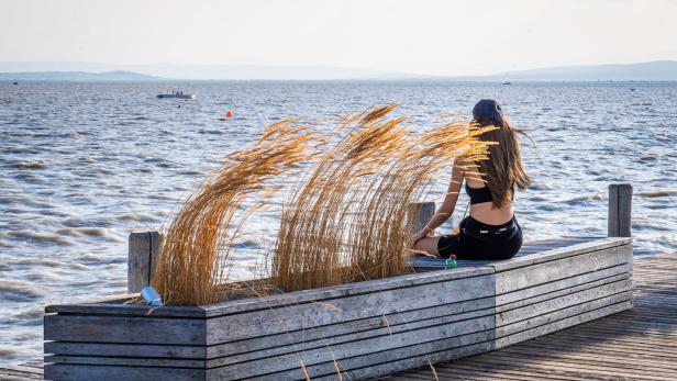 Frau sitzt auf einem Holzsteg am Ufer des Neusiedler Sees