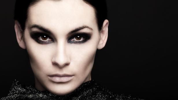 Eine Frau mit dunklem, dramatischem Make-up blickt in die Kamera.