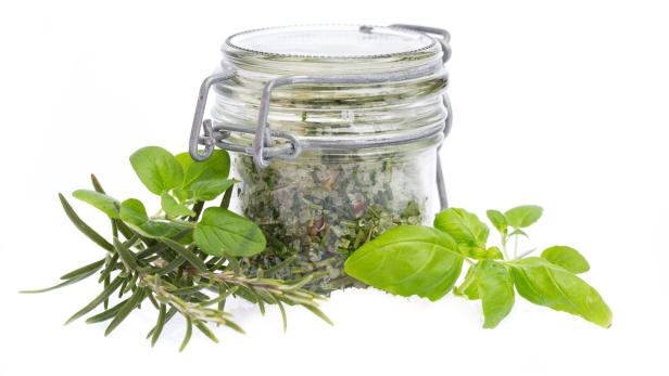 Ein Glas mit Kräutersalz, umgeben von frischen Kräutern wie Rosmarin und Basilikum.