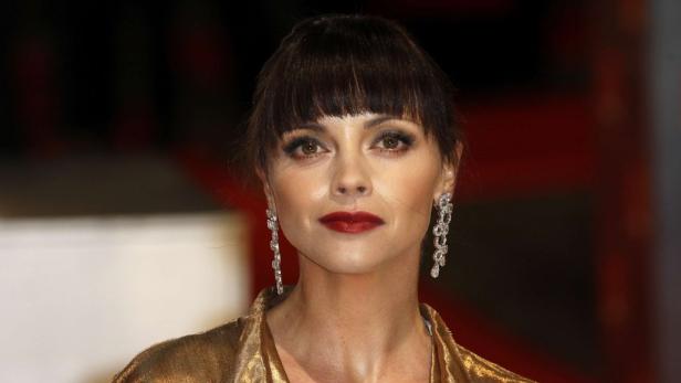 Christina Ricci mit dunklem Pony und roten Lippen trägt lange, glitzernde Ohrringe.