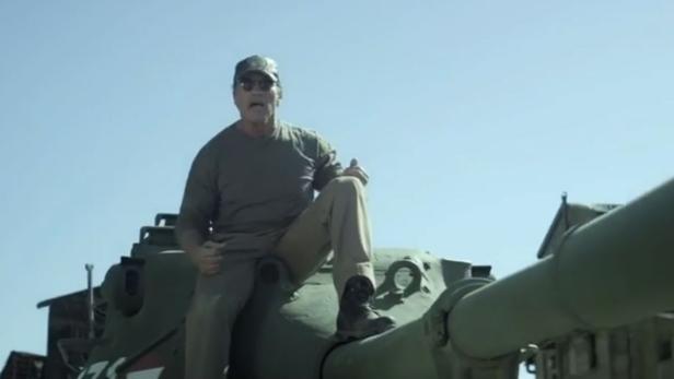 Ein Mann mit Sonnenbrille und Mütze sitzt auf einem Panzer.