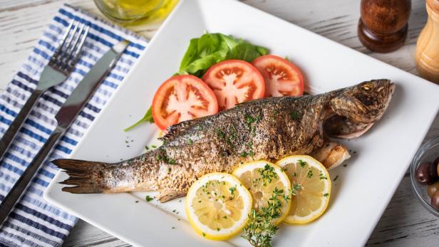 Ein gegrillter Fisch wird mit Zitronen- und Tomatenscheiben auf einem Teller serviert.