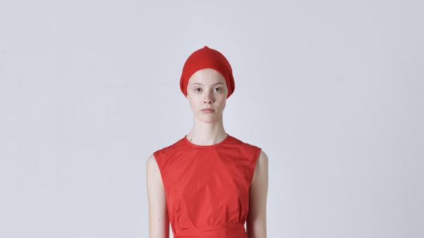 Eine Frau in einem roten Ensemble aus Kleid, Hose, Mütze und Turnschuhen vor einem weißen Hintergrund.