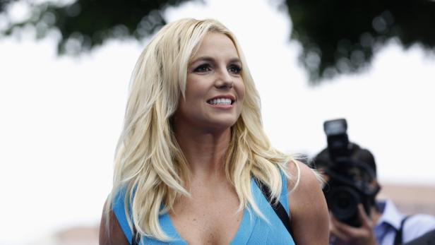 Britney Spears lächelt mit blonden Haaren und blauem Oberteil.
