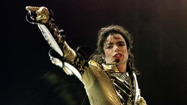 Michael Jackson tritt in einer goldenen Jacke mit erhobenem Arm auf.