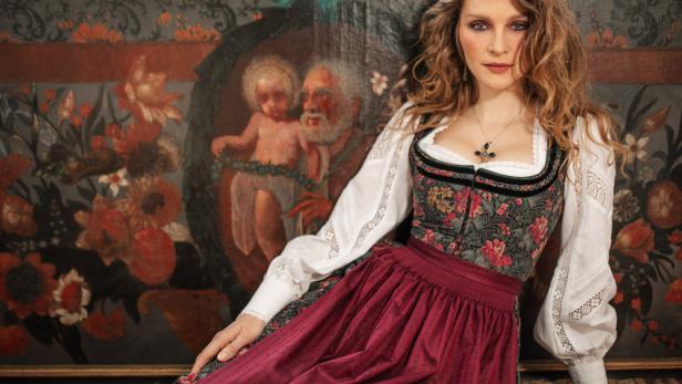 Eine Frau im Dirndl posiert vor einem Gemälde.