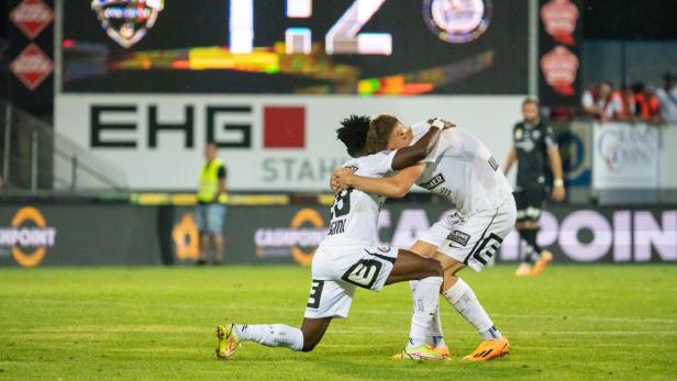 Fußballspieler umarmen sich vor einer Anzeigetafel, die den Spielstand 1:2 zeigt.