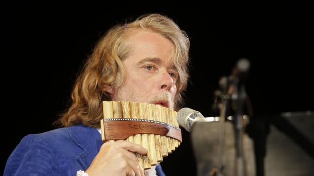 Ein Mann mit langen Haaren spielt eine Panflöte vor einem Mikrofon.