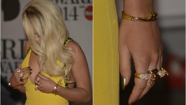 Eine Frau in einem gelben Kleid mit auffälligem Schmuck an Händen und Handgelenken.