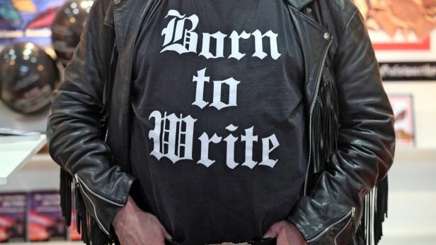 Eine Person mit Lederjacke trägt ein T-Shirt mit der Aufschrift „Born to Write“.