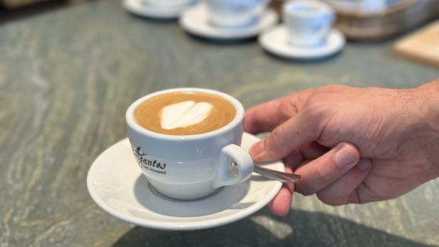 Eine Hand serviert eine Tasse Cappuccino mit Herzmuster auf dem Milchschaum.