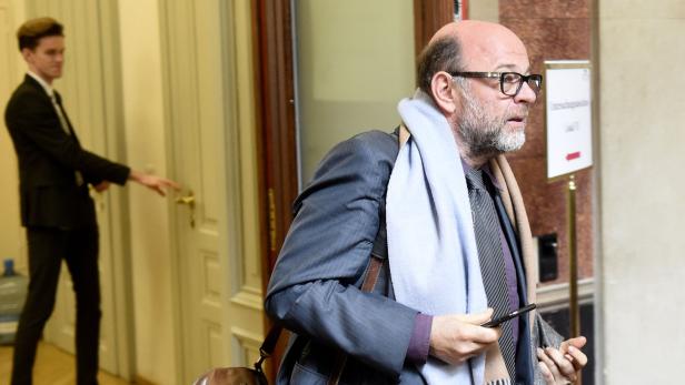 Ein Mann mit Brille und Schal hält ein Smartphone in der Hand, während ein anderer eine Tür öffnet.