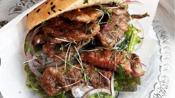 Ein Döner-Sandwich mit Fleisch, Salat und roten Zwiebeln auf einem verzierten Teller.