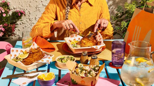 Eine Frau isst ein Wiener Schnitzel im Freien.