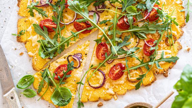 Eine Polenta-Pizza mit Tomaten, roten Zwiebeln und Rucola wird serviert.