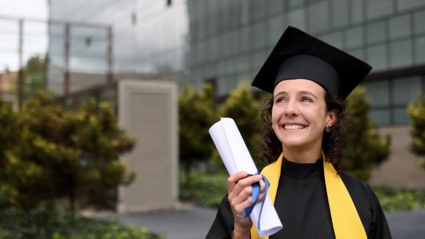 Eine Studentin trägt die Zeremonielle Kleidung mit der schwarzen Kappe zu ihrem Studienabschluss und hält ihr Zeugnis in der Hand