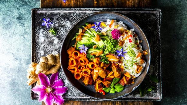 Eine Schüssel mit asiatischem Essen, garniert mit Blüten, auf einem verzierten Tablett.