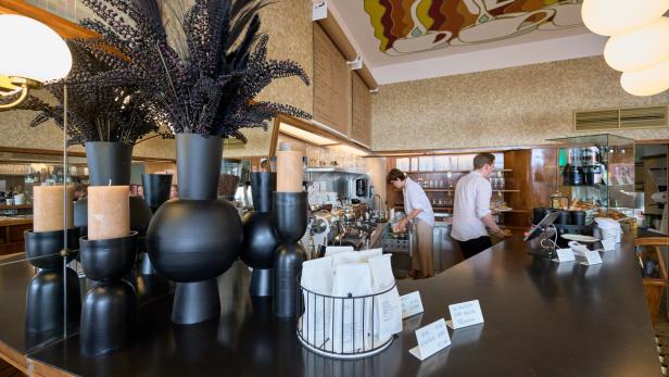 Innenansicht eines Cafés mit dunkler Theke und zwei Angestellten.