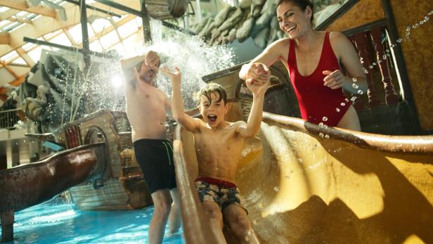 Ein Junge rutscht auf einer Wasserrutsche, während eine Frau und ein Mann zusehen.