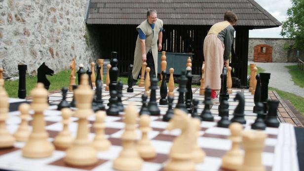 Zwei Personen spielen eine Partie Schach mit übergroßen Figuren im Freien.