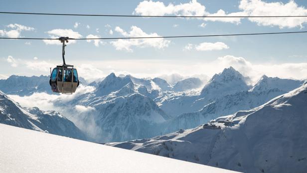 Eine Gondel schwebt vor einer verschneiten Berglandschaft.