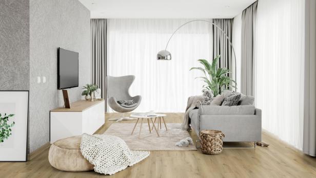 Helles, modern eingerichtetes Wohnzimmer mit grauem Sofa, Sessel, großen Fenstern, Pflanzen und Holzboden.