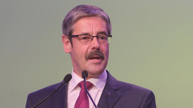 Ein Mann mit Brille und Anzug spricht an einem Rednerpult in zwei Mikrofone.