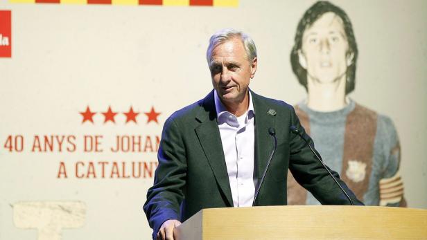 Johan Cruyff bei einer Veranstaltung mit einem Bild von ihm im Hintergrund.