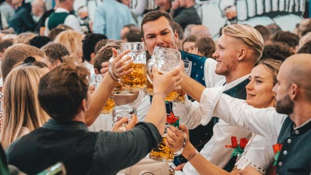 Menschen in Tracht stoßen mit Bierkrügen auf dem Oktoberfest an.