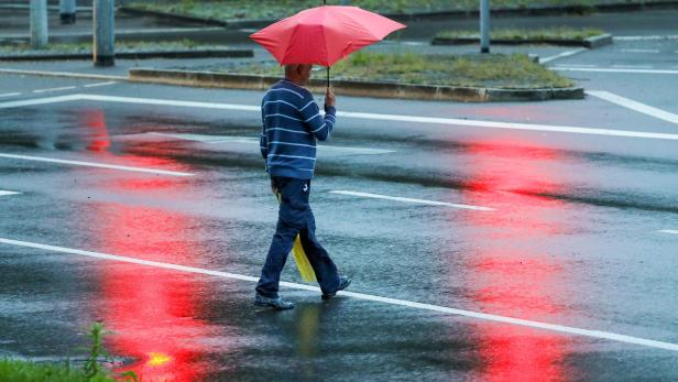 Mann geht mit Regenschirm über eine Straße