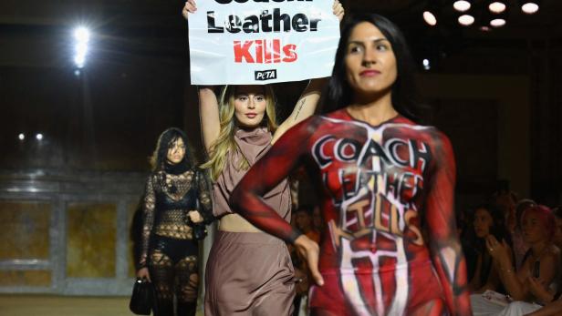 Eine PETA-Demonstration auf einem Laufsteg mit Aktivistinnen, die Schilder und Körperbemalung tragen.