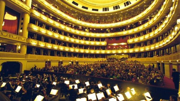 Blick in einen vollbesetzten Zuschauerraum mit Orchestergraben, vermutlich ein Opernhaus.