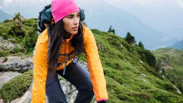 Eine Frau klettert mit Rucksack auf einen Felsen in den Bergen.