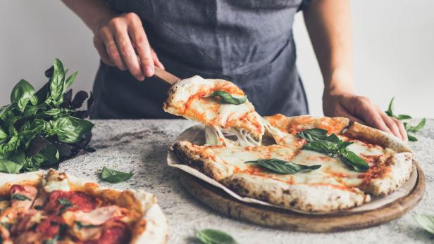 Mann serviert Pizza, Käse zieht Fäden.