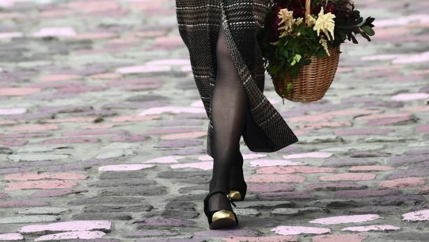 Ein Model mit einem karierten Mantel und einem Blumenkorb auf einem Laufsteg.