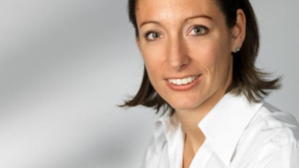 Eine Frau mit braunen Haaren und einem weißen Hemd lächelt.