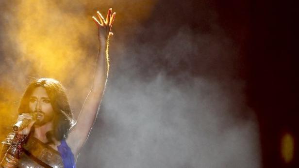 Conchita Wurst singt auf einer Bühne mit erhobenem Arm.