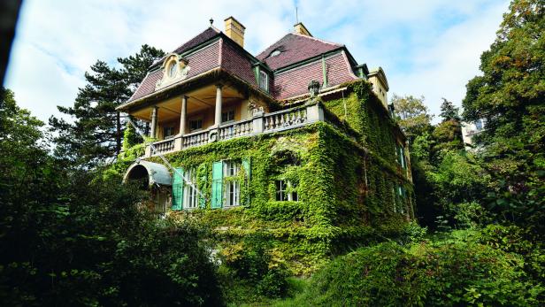 Ein mit Efeu bewachsenes, mehrstöckiges Haus mit einem Balkon und grünen Fensterläden.