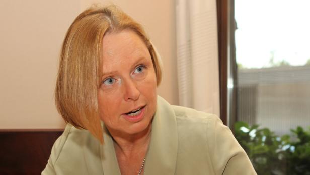 Eine Frau mit blonden Haaren und einem hellgrünen Blazer spricht.