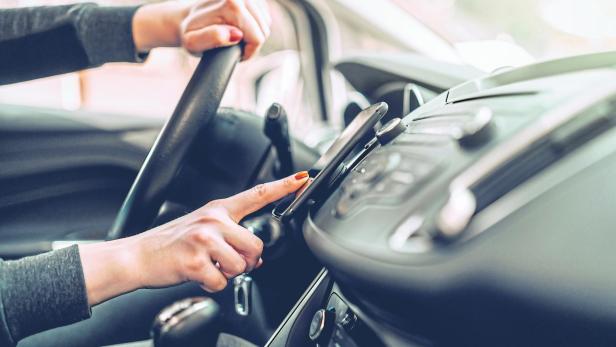 Close up of Caucasian pregnant woman driving car and turning on gps on smart phone. Other hand on steering wheel.