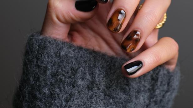 Hand mit braunem und schwarzem Nagellack.