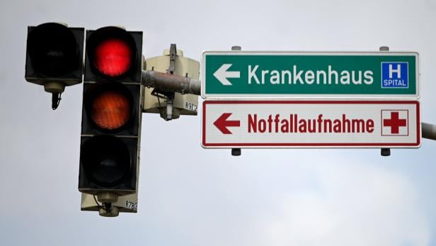 Eine gelb werdende Ampel neben zwei Schildern, die jeweils zu einem Krankenhaus und einer Notaufnahme zeigen.