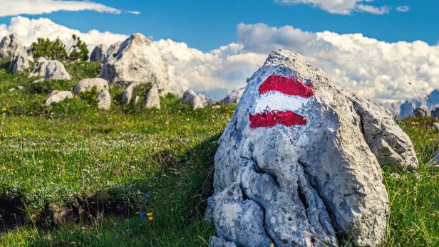 Ein Wegweiser mit rot-weiß-roter Markierung auf einem Felsen in den Bergen.