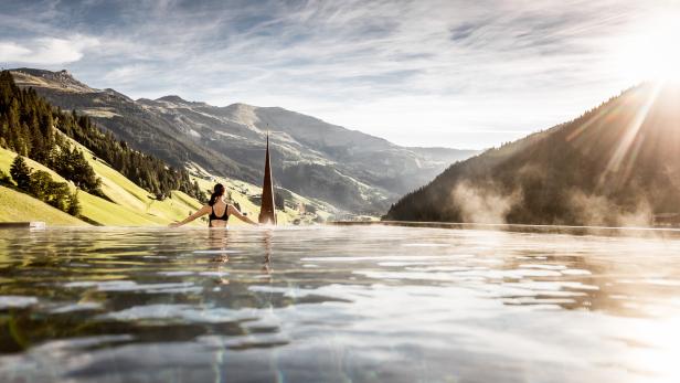 Eine Frau entspannt in einem Infinity-Pool mit Blick auf die Berge.