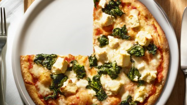 Eine Pizza mit Spinat und Käse auf einem Teller, neben Messer und Gabel.